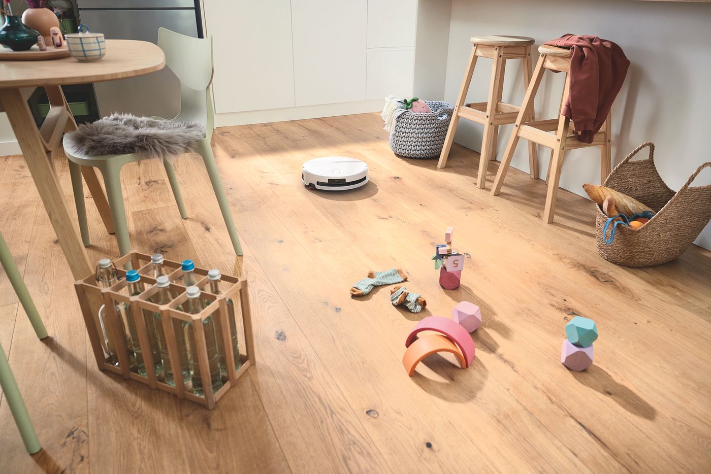 A white Bosch Spotless robot vacuum cleaning a wooden kitchen floor in a bright European-style home.
