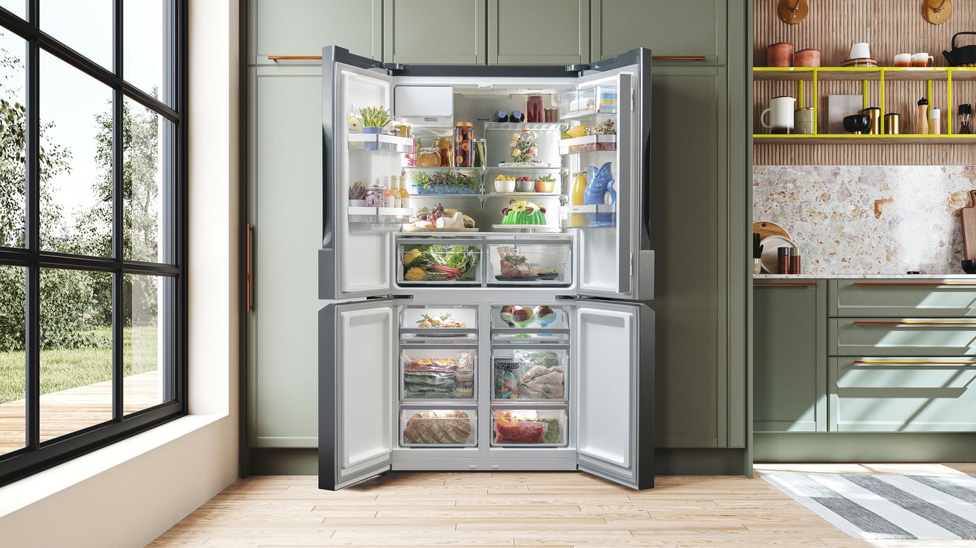 NEFF Multi Door fridge-freezer with all four doors open in a sage-green kitchen, shelves and drawers filled with fresh food.